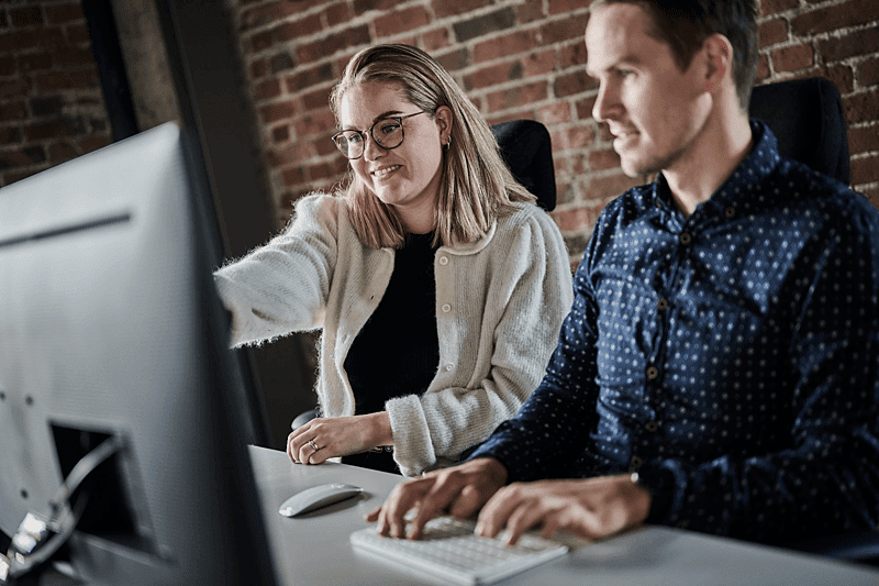 Two colleagues collaborating at a computer, reviewing design files for brand portal integration.